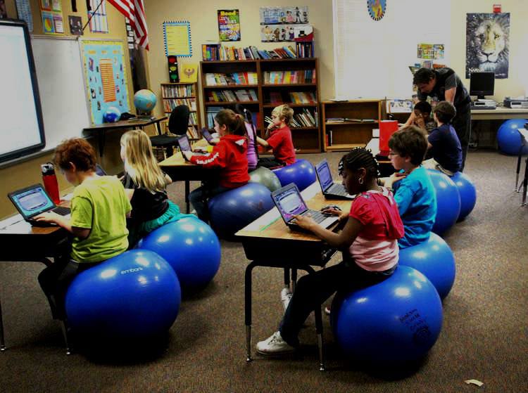 students sitting at their desks in classroom using devices